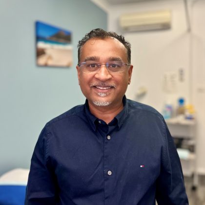 Dr Charles Prasad smiles at the camera with a clinical setting in the background
