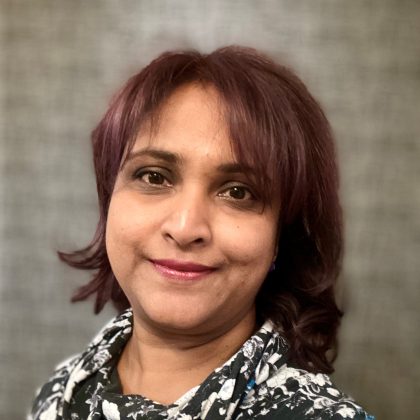 Dr Deepti Prasad smiles at the camera. She has dark red hair and is wearing a black and white blouse