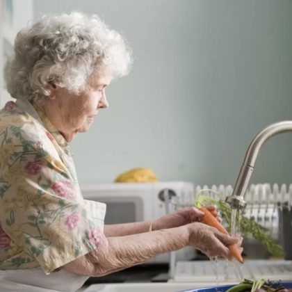 An older woman washes vegetables in her kitchen sink