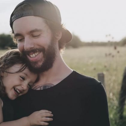 Dad holding young daughter smiling in a field