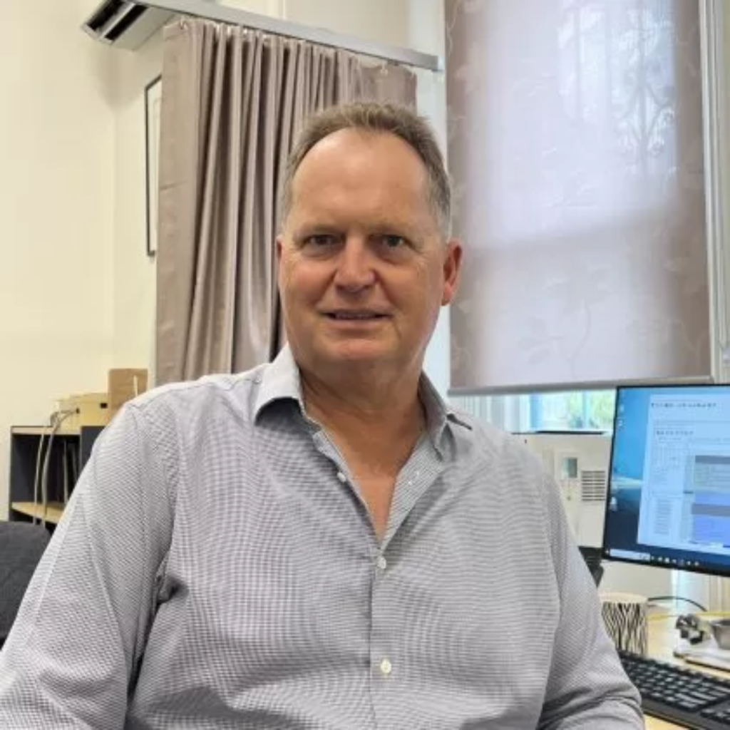 Dr. Simon Moss smiles at the camera. He has short grey hair and is wearing a blue and white shirt