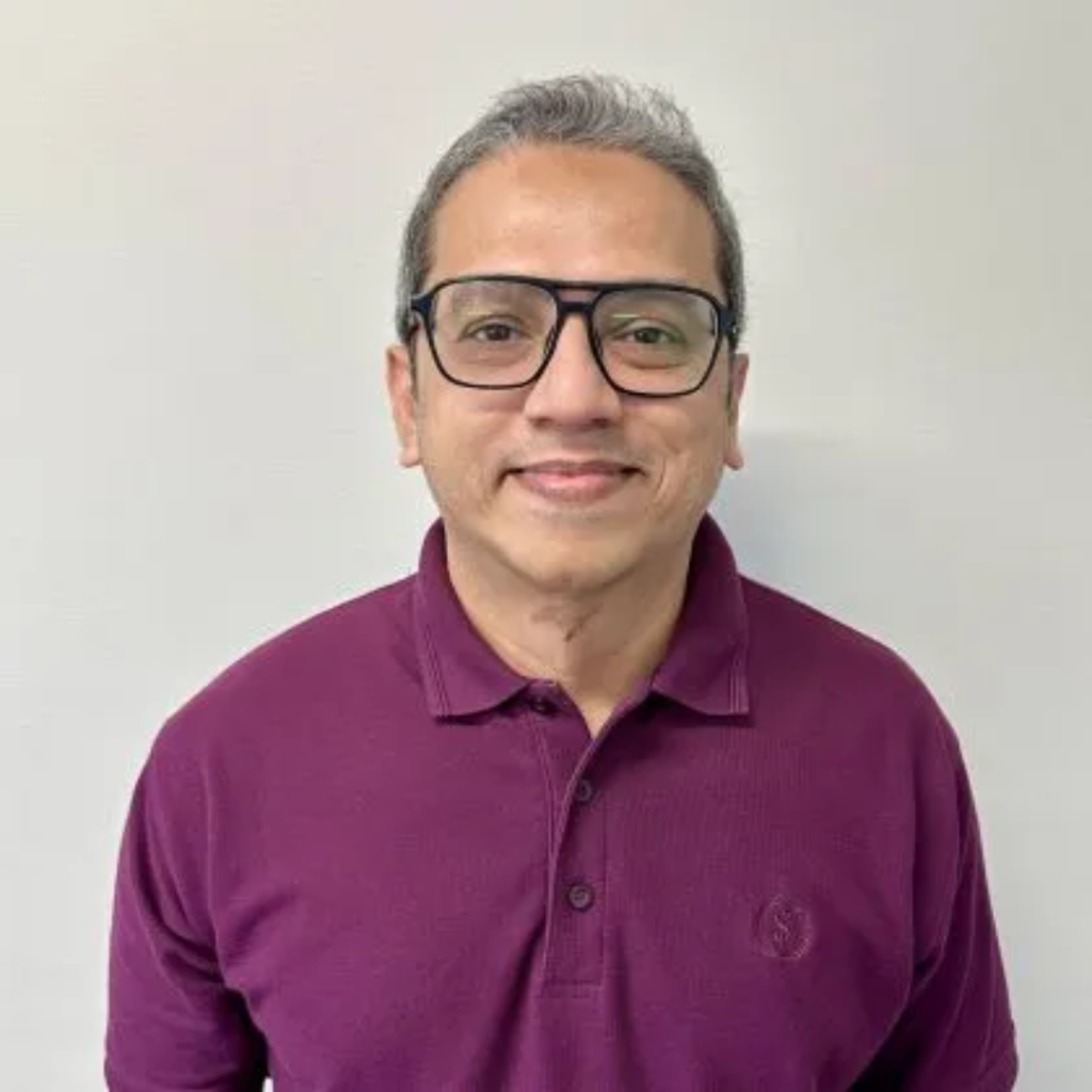 Dr. Adnan Butt smiles at the camera. He has short grey hair and is wearing black glasses